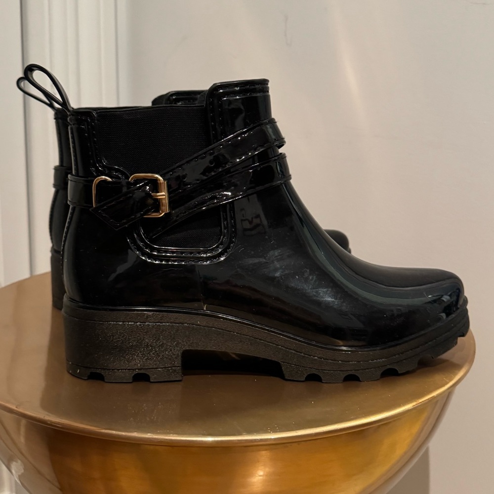 Black, shiny rubber, slip-on, ankle-high rain boots with gold tone buckle detail